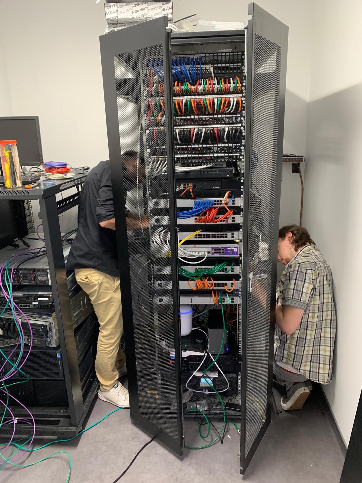 Deux techniciens CN-Tech travaillant sur une baie réseau ouverte chez un client